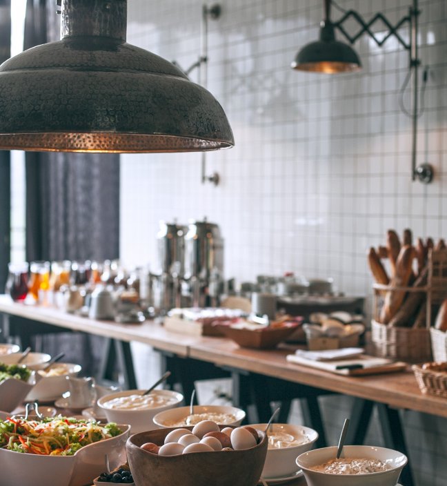 Dining hall with designer lamps and tables with salads, porridge, boiled eggs, baguettes and drinks