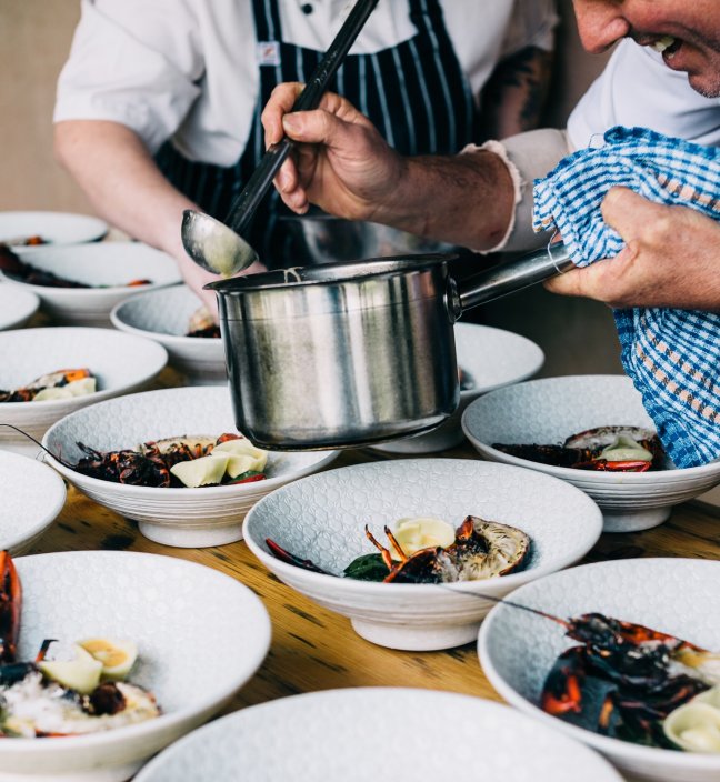 Chef adding sauce to multiple plates with grilled lobster