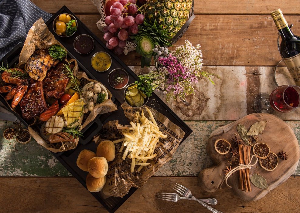 Assorted delicious grilled seafood, meat and fruits, served with multiple sauces and a bottle of wine on the wooden table