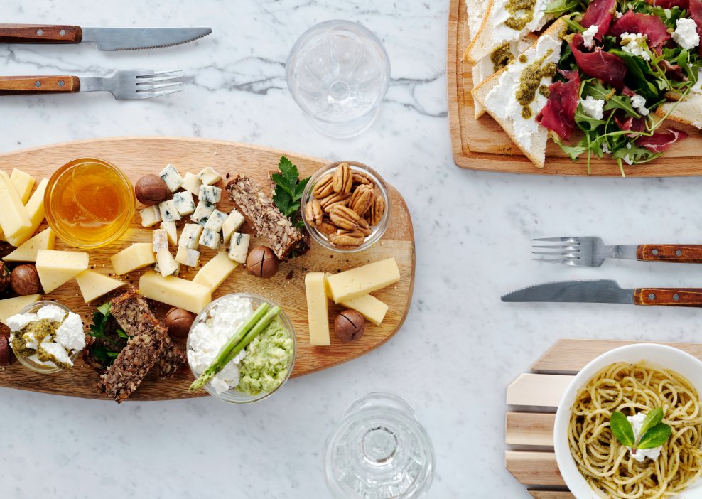 Assorted delicious cheese and nuts, bruschette with yogurt, pesto and bresaola, and a plate of spaghetti on the marble table