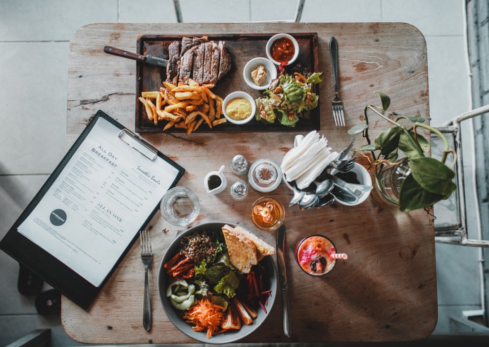 Two dishes at the restaurant table. Grilled steak with sweet potato fries and sauces. Assorted vegetables, buckwheat and crouton, served with balsamic vinegar